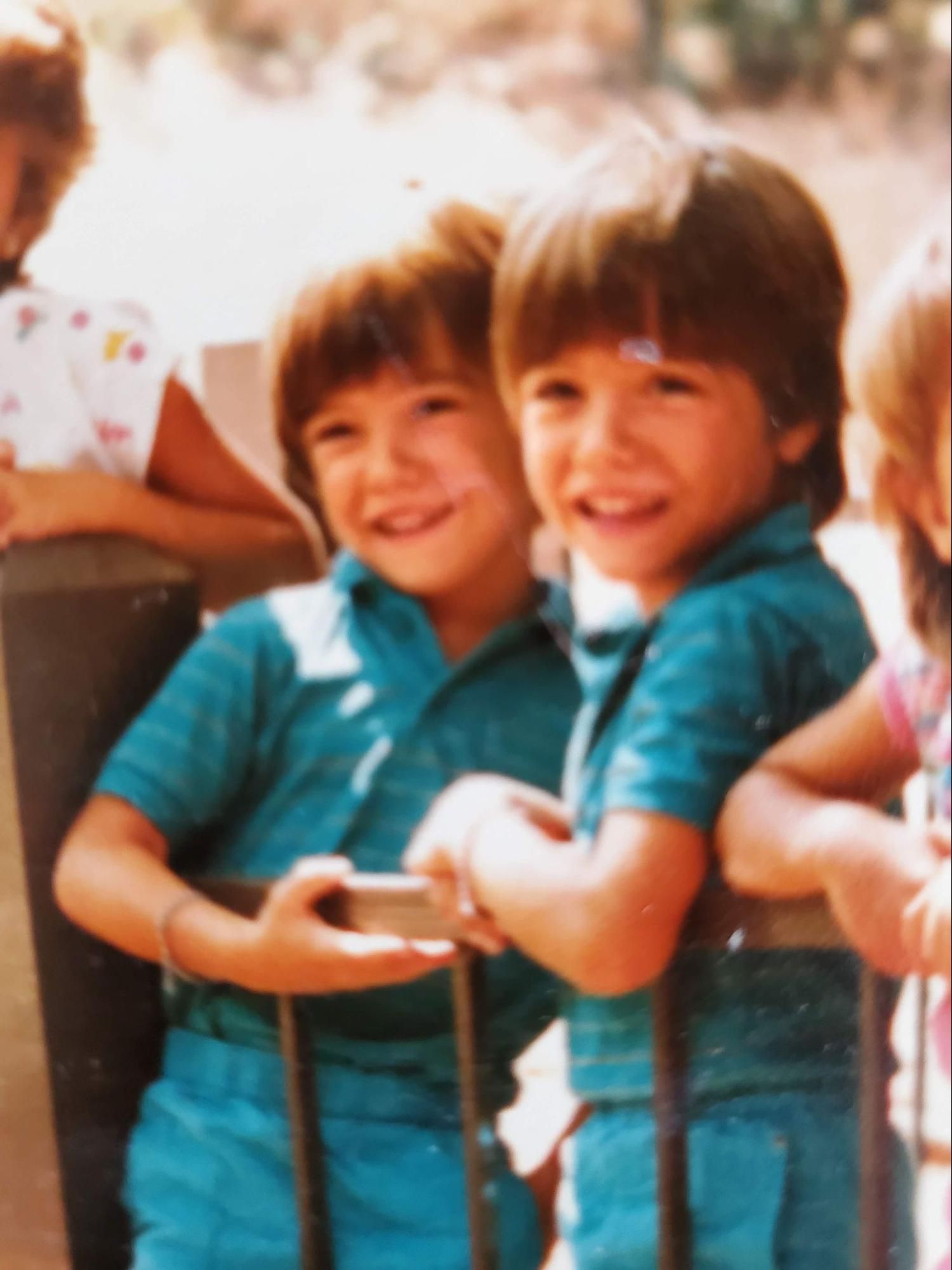 Zac and Jacob as young boys in matching teal shirts, leaning on a railing